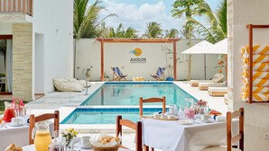 A poolside dining area with a view of the pool, lounge chairs, and a table set for breakfast. - AIOLOS HOTEL & DISCOVERIES (Cruz)