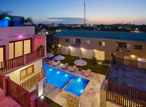 A modern building with a rooftop pool, outdoor seating, and a view of the cityscape at dusk. - AIOLOS HOTEL & DISCOVERIES (Cruz)