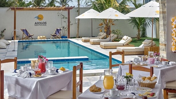 A poolside dining area with tables set for breakfast, overlooking a swimming pool. - AIOLOS HOTEL & DISCOVERIES (Cruz)