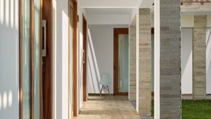 A modern hallway with a glass door, a chair, and stone pillars. - AIOLOS HOTEL & DISCOVERIES (Cruz)