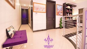A hallway with a purple sofa, a staircase, and a chandelier. - 🕯Versaille’s Residence ™ (McAllen)