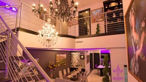 A multi-level living space with a staircase, a chandelier, a dining area, and a painting. - 🕯Versaille’s Residence ™ (McAllen)