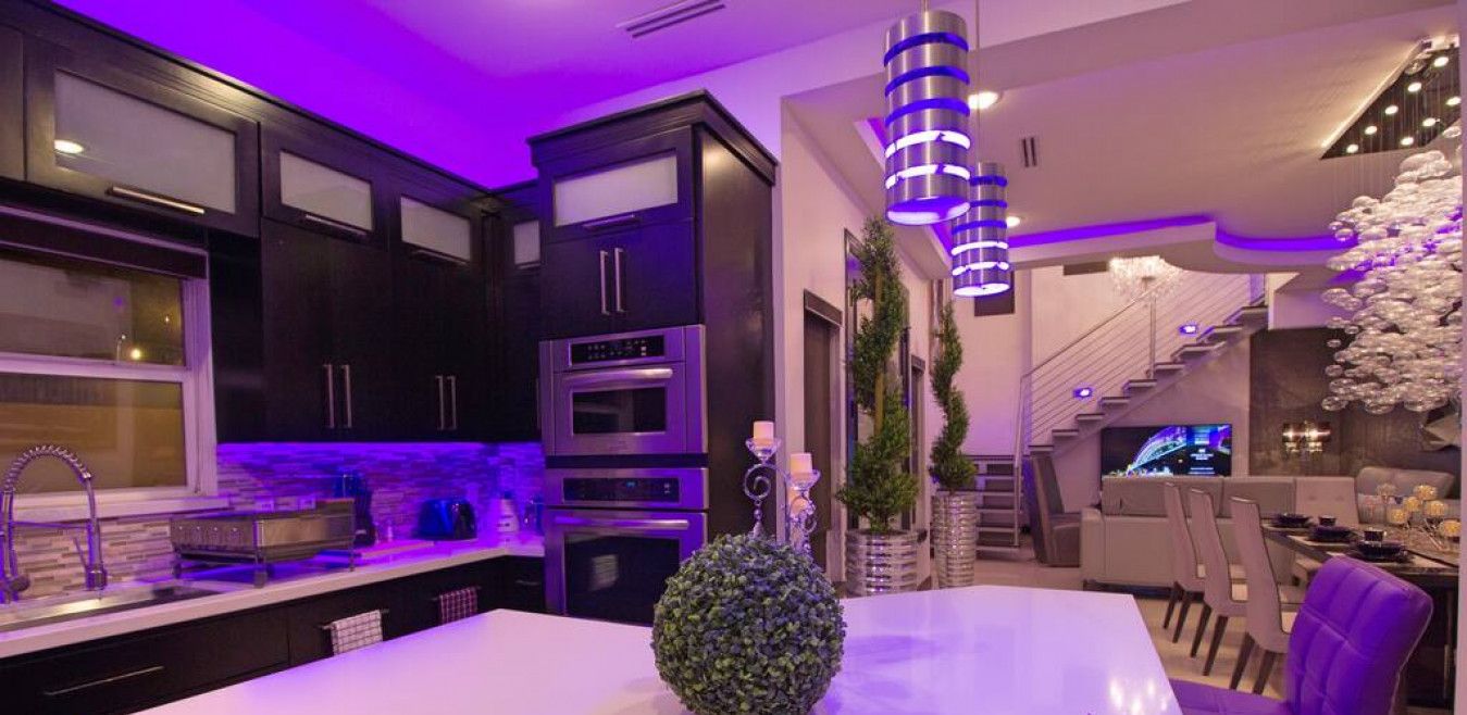 A modern kitchen with dark cabinetry, a central island, and a dining area with purple chairs.