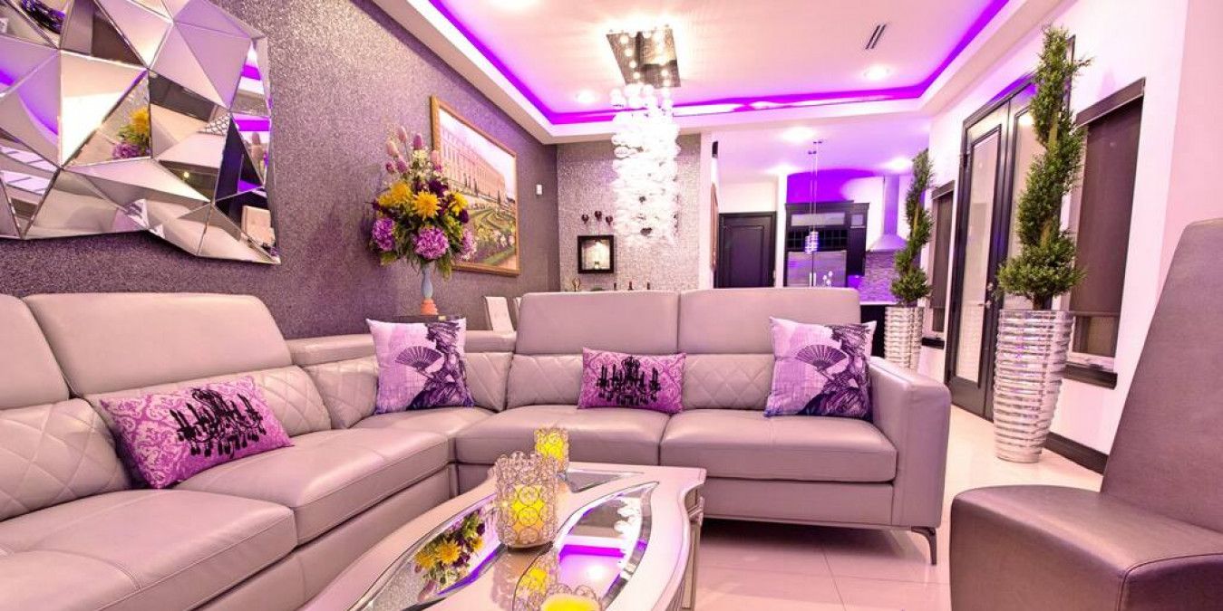 A modern living room with a sectional sofa, a glass coffee table with decorative items, and a chandelier.