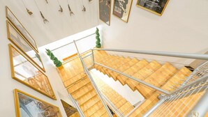 Una escalera con escalones de madera y barandillas de metal, que conduce a una zona de desembarco con cuadros enmarcados y una pequeña planta verde.
