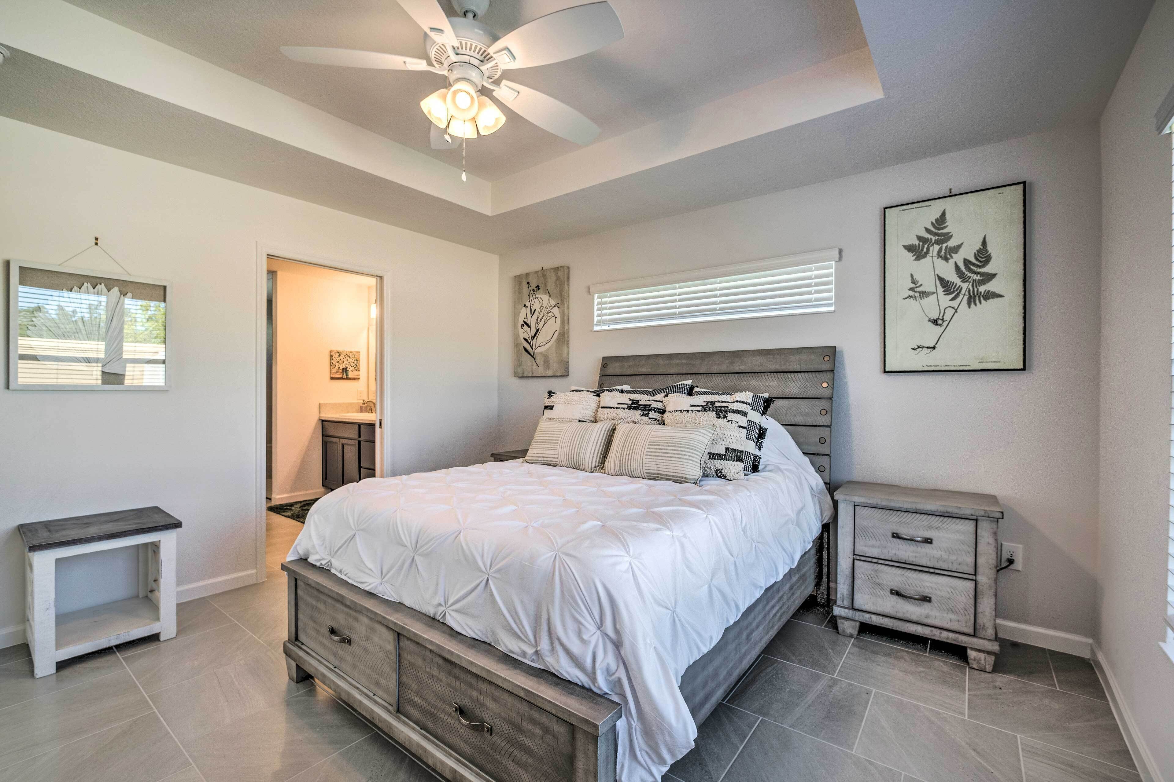 A bedroom with a bed, bedside tables, a ceiling fan, artwork, and a window with blinds.