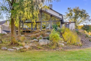 A modern house with a glass conservatory, surrounded by a landscaped garden with rocks and trees.