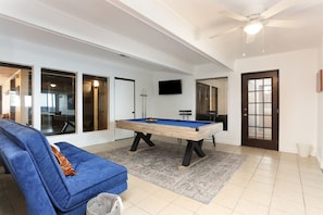 Amplia sala de estar con mesa de billar, un sofá azul y un ventilador de techo.