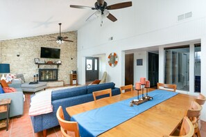 Un salon spacieux doté d’une cheminée, d’un mur en pierre et d’une grande table à manger recouverte de nappes bleues.