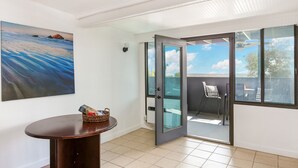Ein Zimmer mit Meerblick, eine Glastür zum Balkon, ein kleiner Tisch mit einem Korb und ein Sessel.
