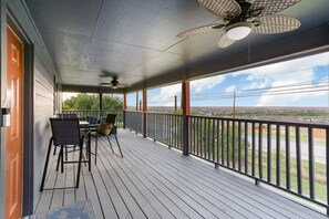 Une véranda abritée avec une table et des chaises, un ventilateur de plafond et une vue sur un quartier résidentiel.