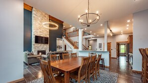 A spacious dining area with a large wooden table and chairs, a fireplace, and a staircase leading to an upper level.