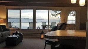 Een gezellige woonkamer met een groot raam met uitzicht op een waterpartij, een eethoek met tafel en stoelen, en een bank.