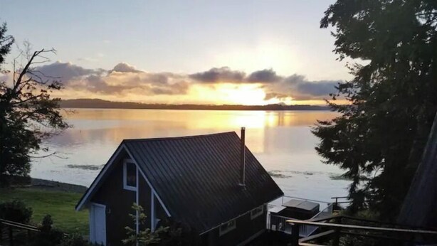 Een vakantiehuisje met een metalen dak, uitkijkend op een rustig meer bij zonsondergang.