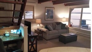 Een gezellige woonkamer met een bank, een salontafel en een televisie. Er is een raam met uitzicht op de omgeving.