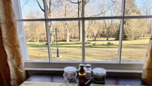 A dining table with two plates and a glass, set against a window with a view of a park. - The Sunnyside Sisters Bed and Breakfast (Clarksville)