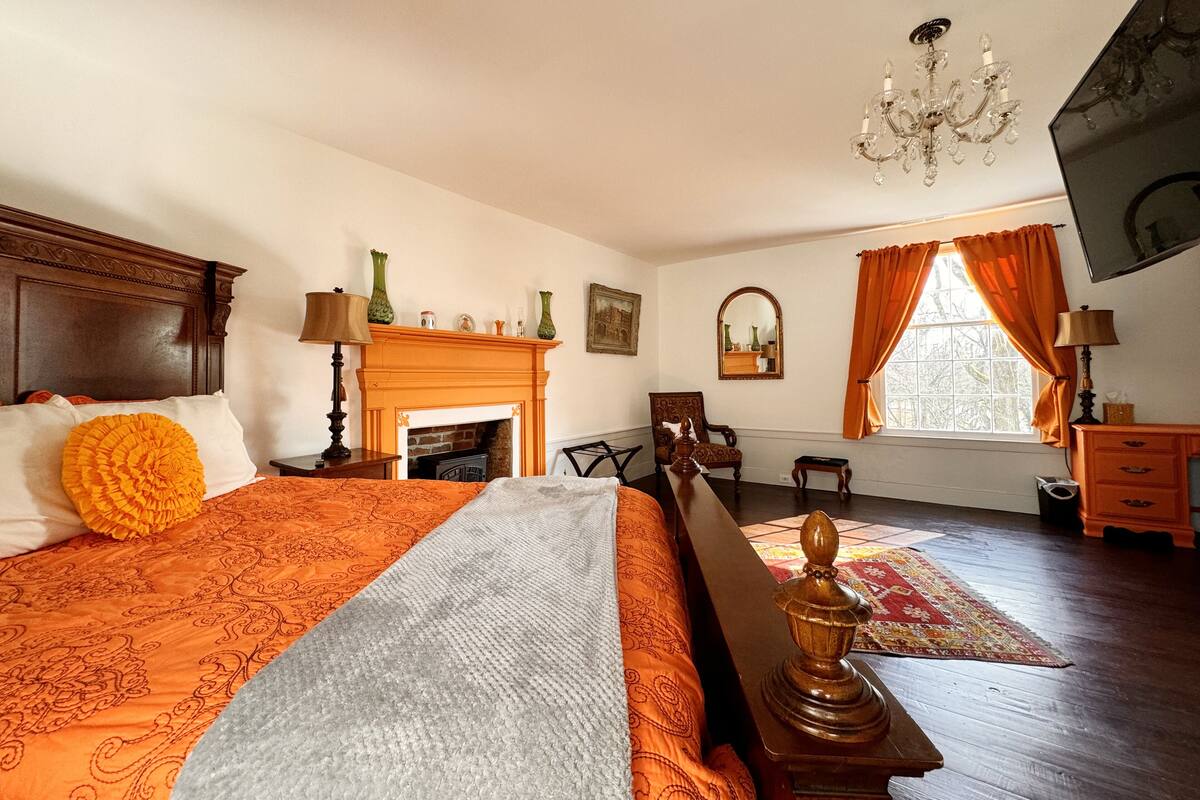Un dormitorio con una cama grande, una chimenea, un candelabro y un ventanal con cortinas.