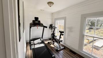 A room with a treadmill, stationary bike, and a window with a view of a park.