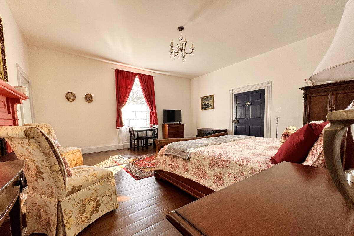 Un dormitorio con cama, una silla, un escritorio, un televisor y una puerta.