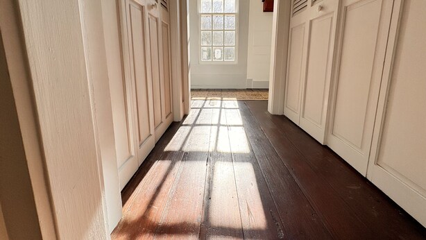 A hallway with wooden floors and white walls, leading to a window with a view of trees. - The Sunnyside Sisters Bed and Breakfast (Clarksville)