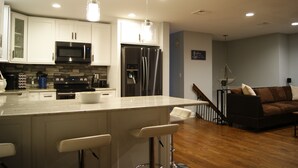 A modern kitchen with white cabinetry, stainless steel appliances, and a bar area with stools. - BestOBothWorlds*2GWifi@HandcraftedWoodTerrace~Firepit#GameRoom (Jefferson)