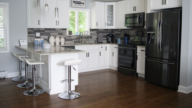 A modern kitchen with white cabinets, stainless steel appliances, and a bar area with stools. - BestOBothWorlds*2GWifi@HandcraftedWoodTerrace~Firepit#GameRoom (Jefferson)