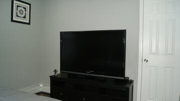 A bedroom with a bed, a black entertainment center with a TV, a white door, and a framed picture on the wall.