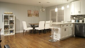 A modern kitchen with white cabinetry, a dining area with white chairs, and a built-in island with bar stools. - BestOBothWorlds*2GWifi@HandcraftedWoodTerrace~Firepit#GameRoom (Jefferson)