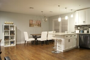 A modern kitchen with white cabinetry, a dining area with white chairs, and a built-in island with bar stools.