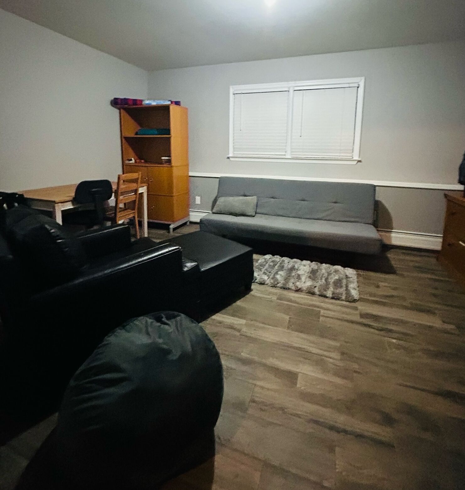 Una sala de estar con un sofá gris, un sillón negro, un aparador de madera y una mesita.