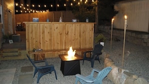 An outdoor seating area with a wooden bar, a fire pit, and two chairs. - BestOBothWorlds*2GWifi@HandcraftedWoodTerrace~Firepit#GameRoom (Jefferson)