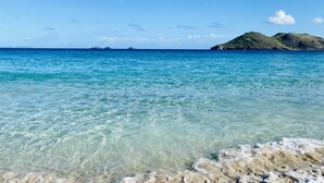 A clear view of a beach with calm waters, distant islands, and a clear sky.