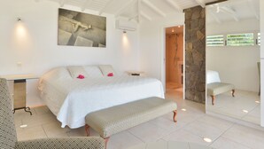 A bedroom with a large bed, a bench, a mirror, and a stone wall.