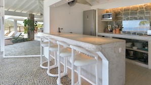 A modern kitchen with a stone wall, white bar stools, and a bar counter.