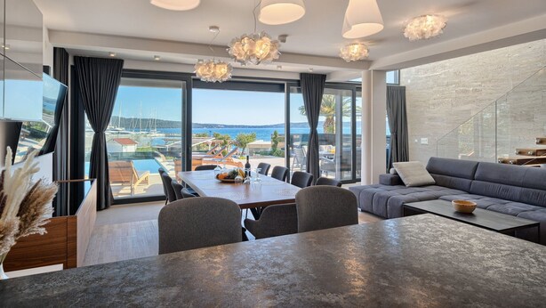 A modern living room with a dining area, large windows with a view of the sea, and a stone wall. - Luxury Villa Imperio with Pool (Kaštel Gomilica)