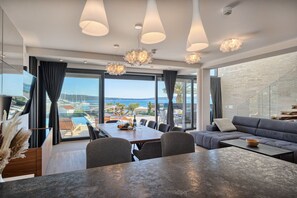 Ein modernes Wohnzimmer mit Essbereich, großen Fenstern und Meerblick, sowie einer Steinwand.