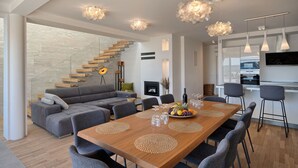 A modern living space with a wooden dining table, grey sofas, and a staircase with wooden steps. - Luxury Villa Imperio with Pool (Kaštel Gomilica)