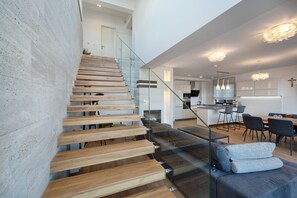 Ein modernes Interieur mit einer Holztreppe, einer Glastrennwand, einem grauen Sofa und einer Küchenzeile.