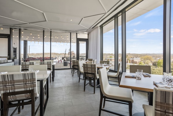 A modern dining area with large windows, tables, and chairs.