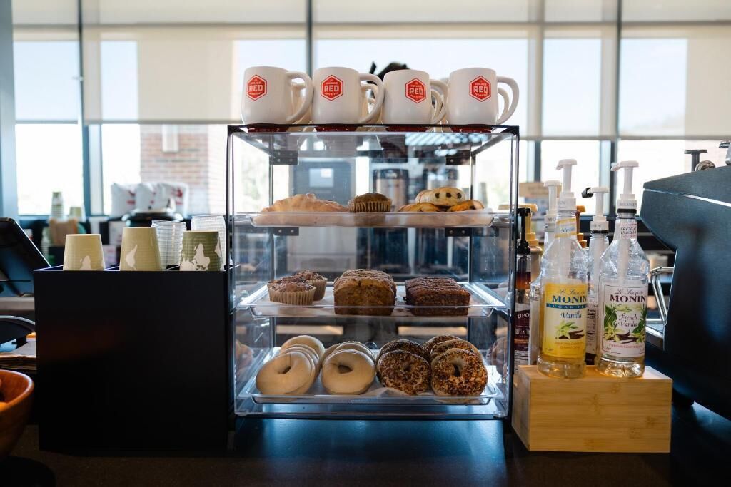 Una vitrina con diversos pasteles y donas, una estación de café con tazas y botellas de sirope Monin.
