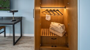 A wooden wardrobe with a hanging rod, a bench, and a small table with a lamp.