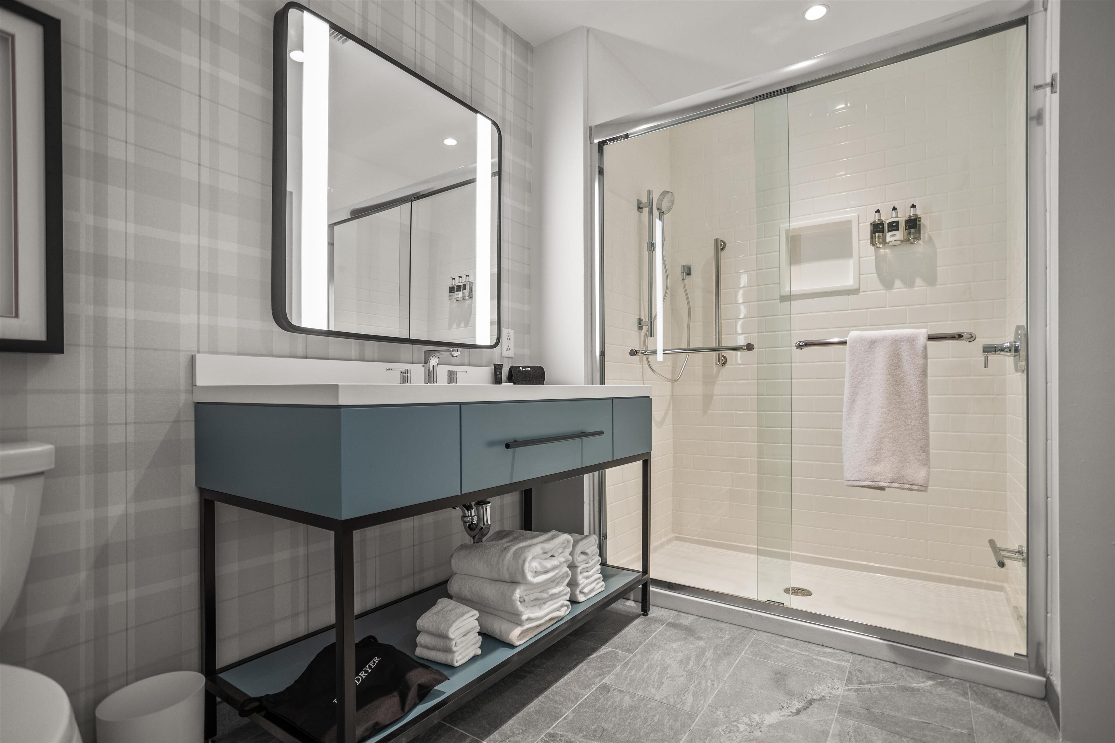 A modern bathroom with a glass-enclosed shower, a vanity with a mirror, and neatly folded towels on a shelf.