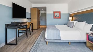 A hotel room with a bed, a desk, a chair, a TV, and a framed picture on the wall.