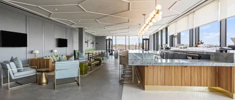 Un moderno vestíbulo de hotel con una zona de bar central, arreglos de asientos y grandes ventanales que ofrecen vistas.