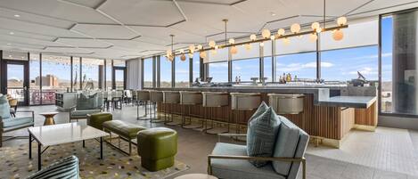A modern lounge area with seating, a bar, and large windows offering a view of the cityscape.