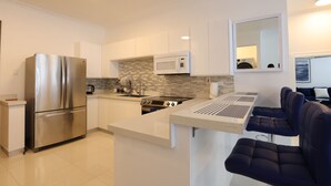 A modern kitchen with a stainless steel refrigerator, a microwave, and a built-in stove. There is a seating area with a table and chairs. - luxury Condo at Kensington Gates (Kingston)