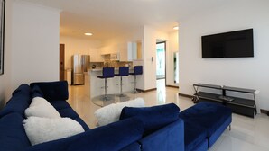 A modern living room with a blue sofa set, a glass coffee table, and a flat-screen TV mounted on the wall. - luxury Condo at Kensington Gates (Kingston)