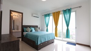 A bedroom with a bed, a nightstand, a window with curtains, and a view of the city. - luxury Condo at Kensington Gates (Kingston)