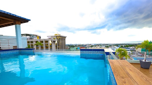 A rooftop pool with a wooden deck, surrounded by buildings and palm trees. - luxury Condo at Kensington Gates (Kingston)