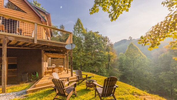 Une cabane en bois dotée d’une terrasse, de meubles de jardin et offrant une vue panoramique sur une colline boisée.